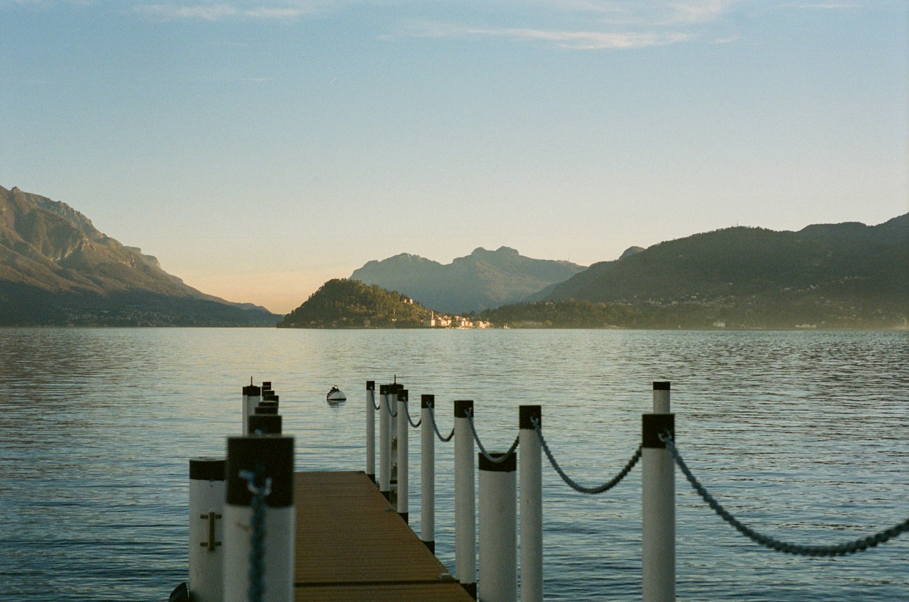 A wooden jetty extending toward still water and layered mountains on Lake Como