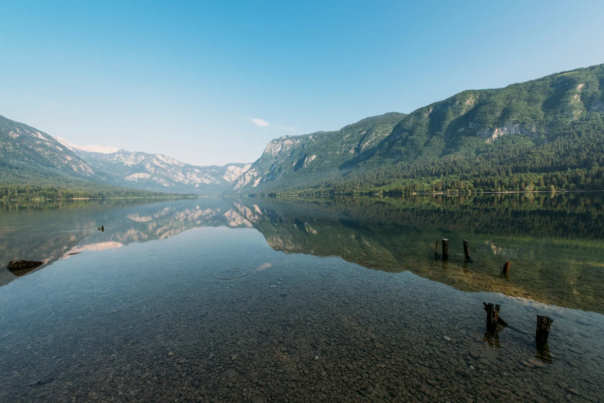 Still mountain water reflecting a wide valley, with clear shallows in the foreground.